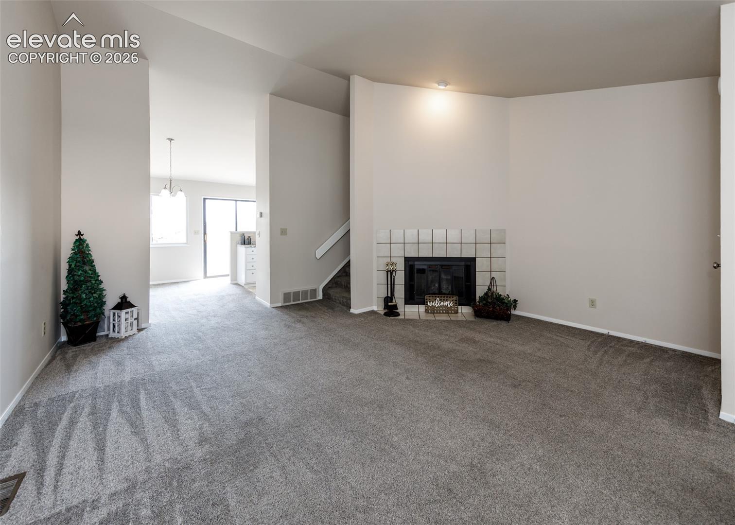 Recessed lighting, tiled fireplace surround, carpeted flooring, staircase, and a doorway opening to an additional space with a window