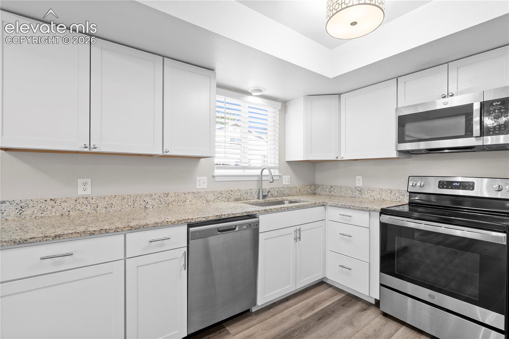 Kitchen featuring white shaker-style cabinetry, stone-finish countertops, stainless steel appliances, wood-finish flooring, and recessed ceiling lighting