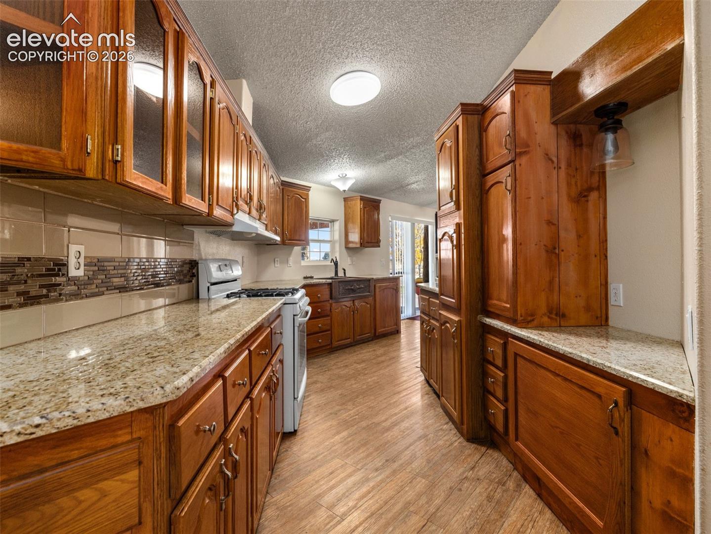 Kitchen featuring wood cabinetry, stone-finish countertops, tile backsplash, wood-finish flooring, and built-in lighting