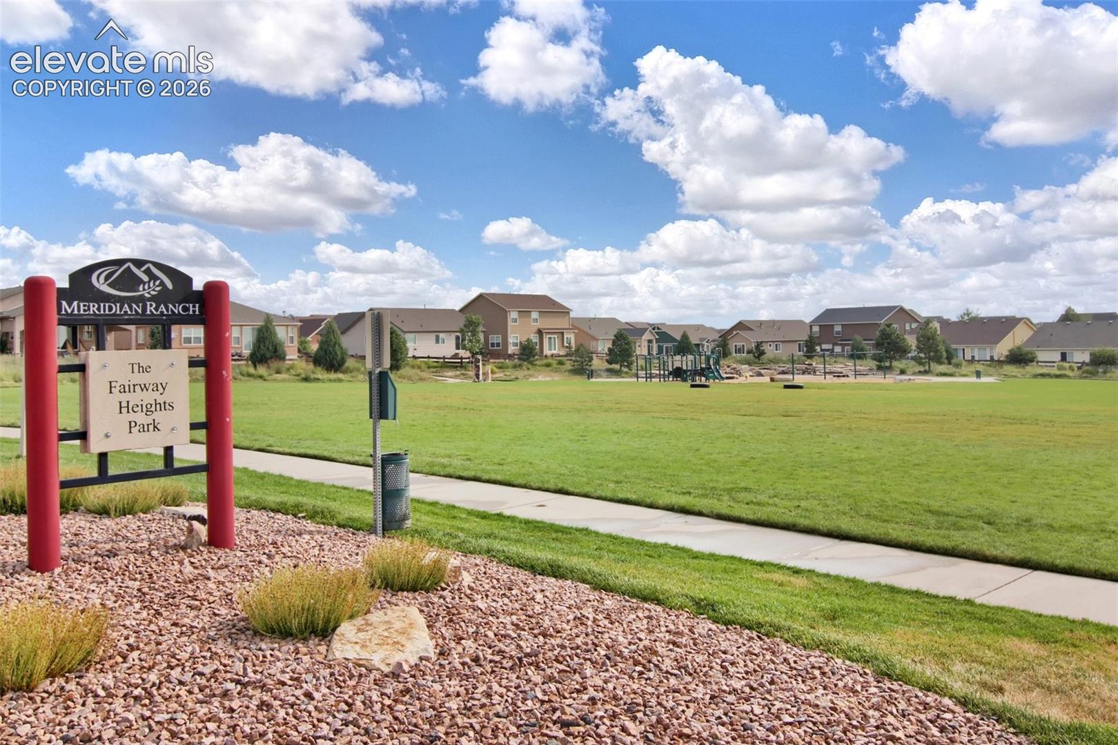 Fairway Heights Park featuring a manicured grass field, concrete walking path, and dedicated playground equipment