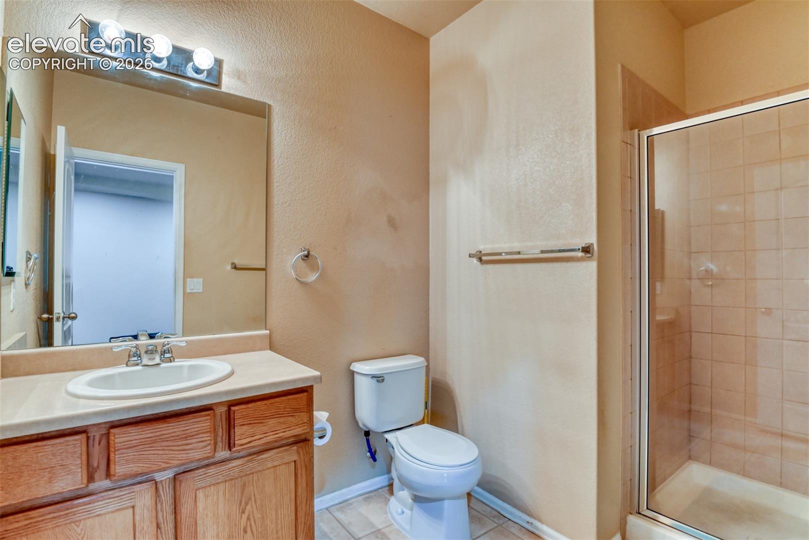 Bathroom featuring a wood vanity with a solid-surface countertop, an integrated oval sink, a glass-enclosed shower with tiled walls, and a wall-mounted light fixture