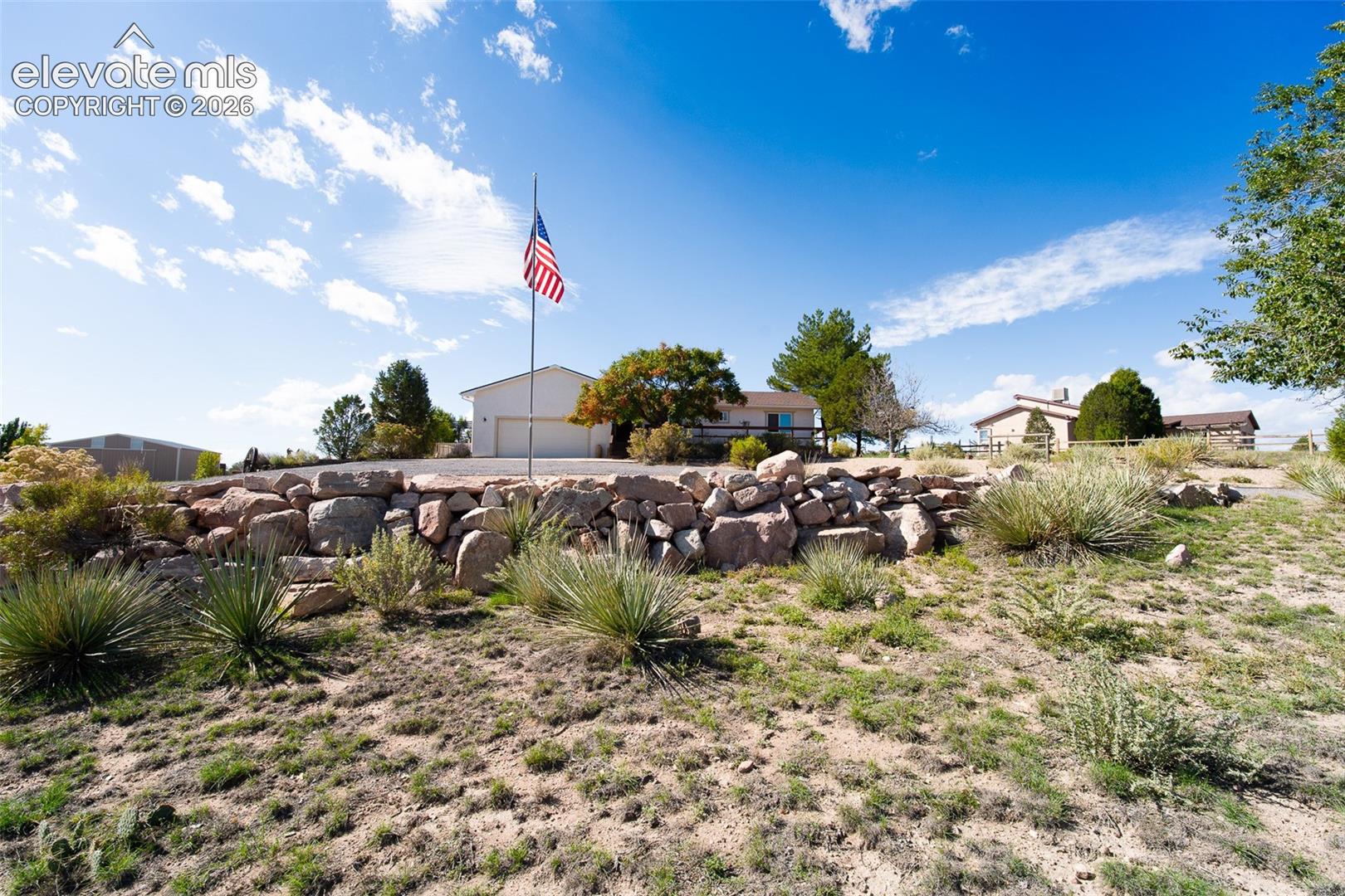 Exterior landscape featuring a tiered natural stone retaining wall, desert-style xeriscaping, and an attached multi-car garage