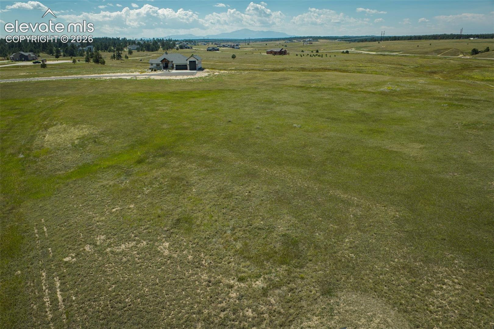 Expansive undeveloped land with a distant single-story residence and visible mountain range