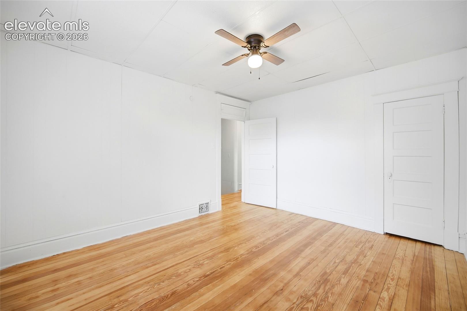 Interior room featuring wood-finish flooring, white walls, five-panel interior doors, and a ceiling-mounted light fixture with a four-blade fan