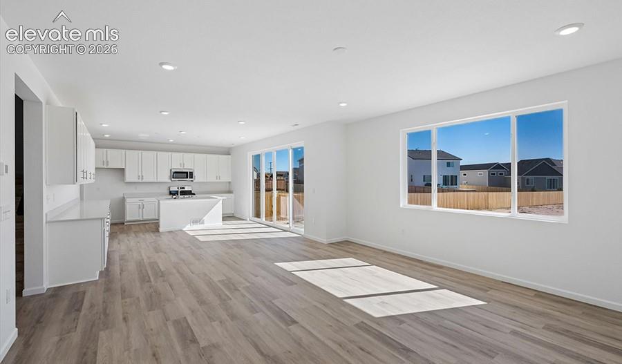 Open-concept interior featuring wood-finish flooring, recessed lighting, white cabinetry, a center kitchen island, and large windows
