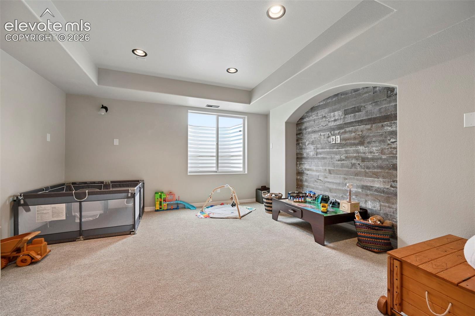 Recessed ceiling lighting, tray ceiling, and an arched alcove featuring a horizontal wood-plank accent wall
