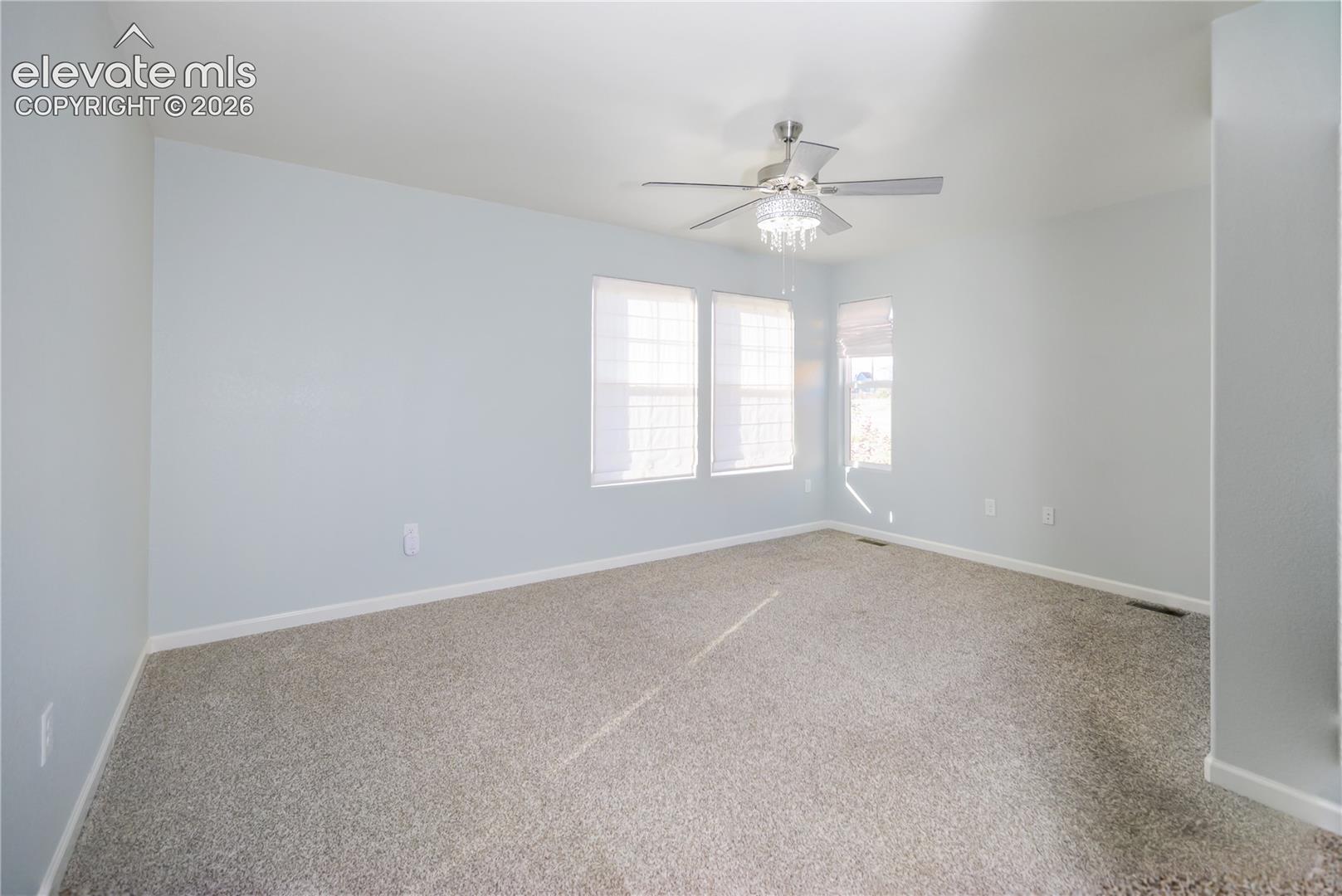 Interior space featuring neutral wall tones, wall-to-wall carpeting, multiple windows, and a ceiling fan with integrated lighting