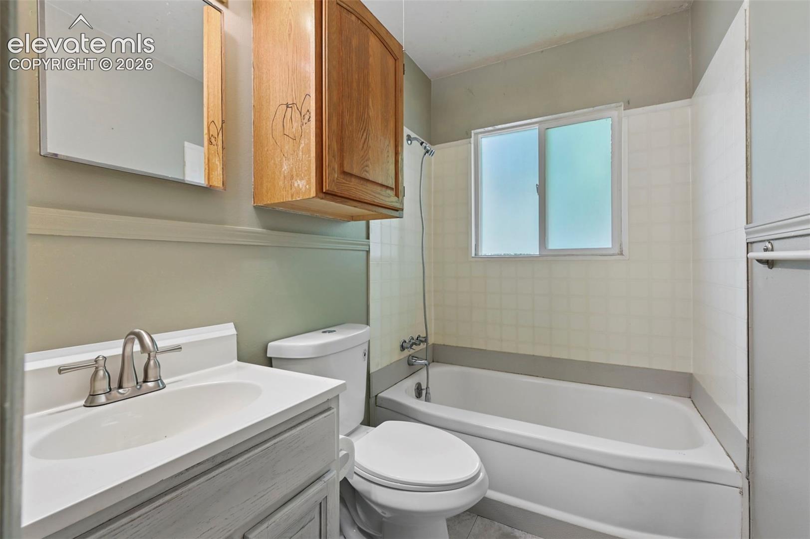 Bathroom featuring a white bathtub, frosted window, white tiled surround, white vanity with integrated sink, and brushed nickel faucet