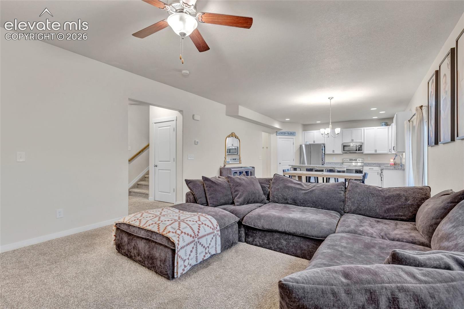 Spacious living area with ceiling fan and recessed lighting, opening to a kitchen featuring white cabinetry, stainless steel appliances, and a central island with seating
