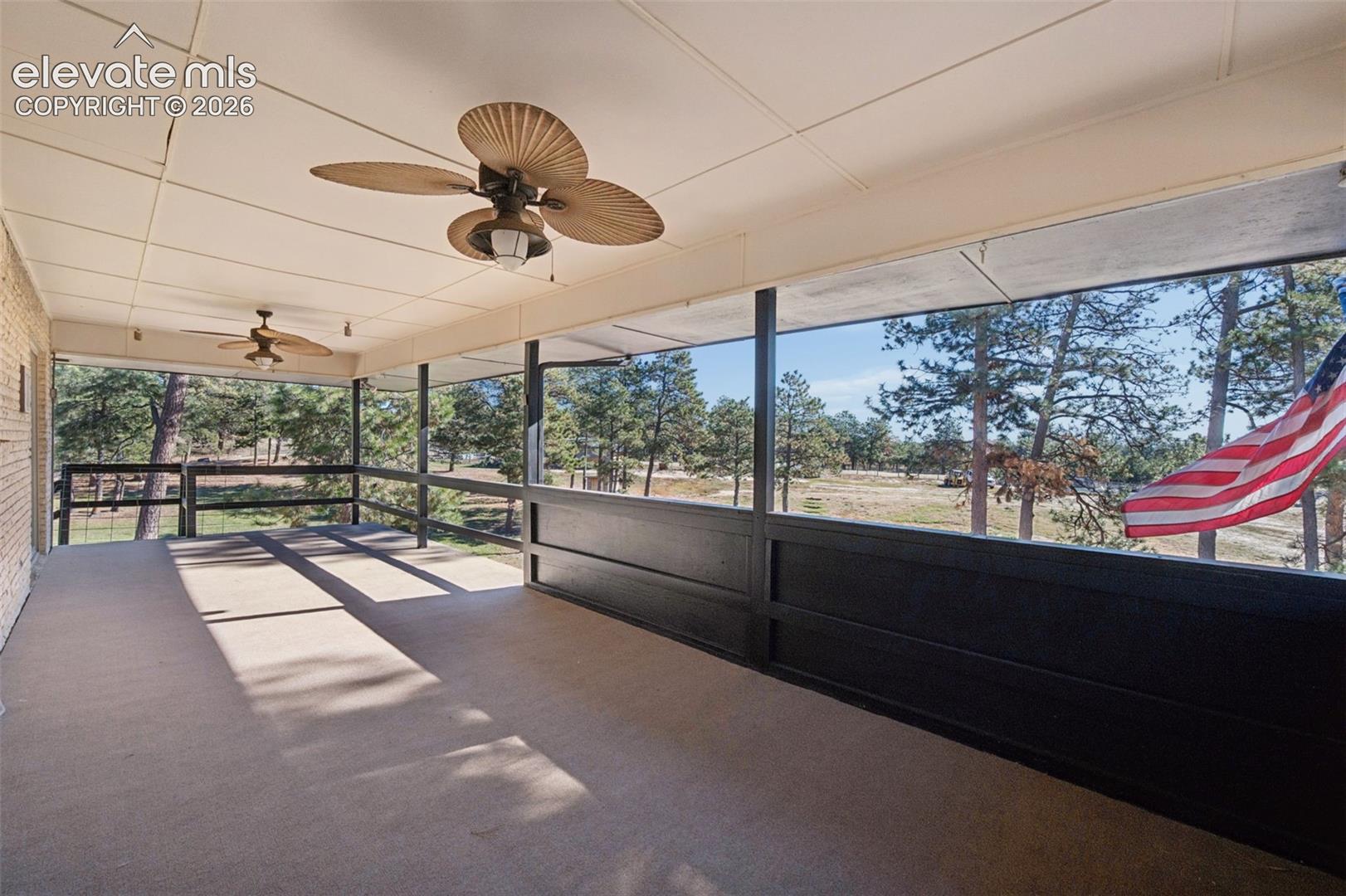 Covered porch featuring dual ceiling fans, solid paneling, and an exterior railing