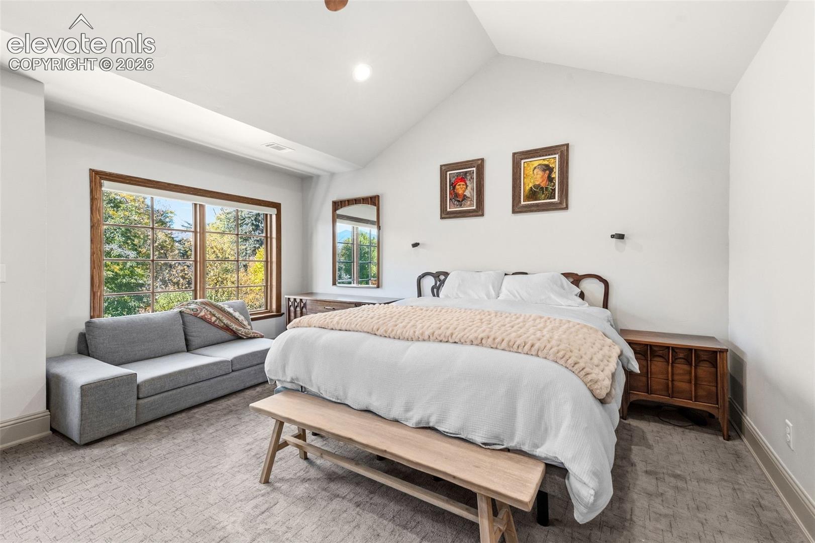 Vaulted ceilings, large multi-pane windows with wood trim, wall-mounted light fixtures, and wall-to-wall carpeting