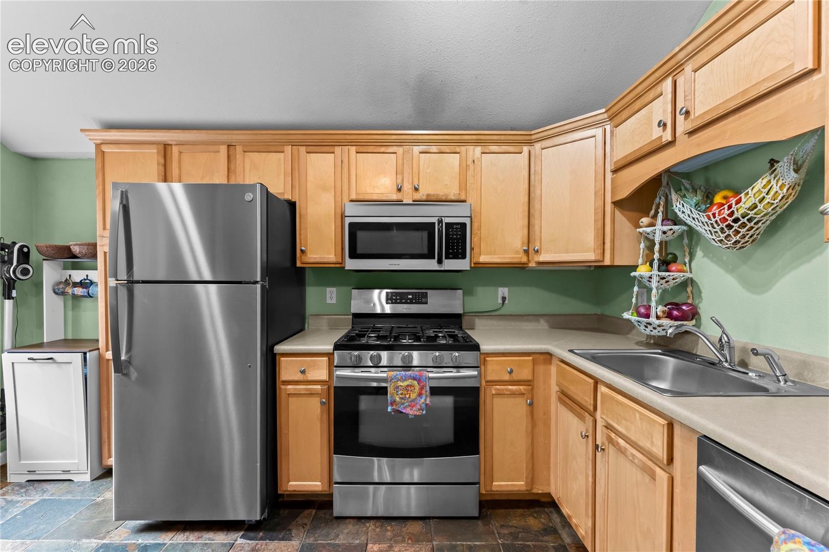 Kitchen featuring light-finish cabinetry, stainless steel appliances, a built-in microwave, stone-finish countertops, and an undermount sink