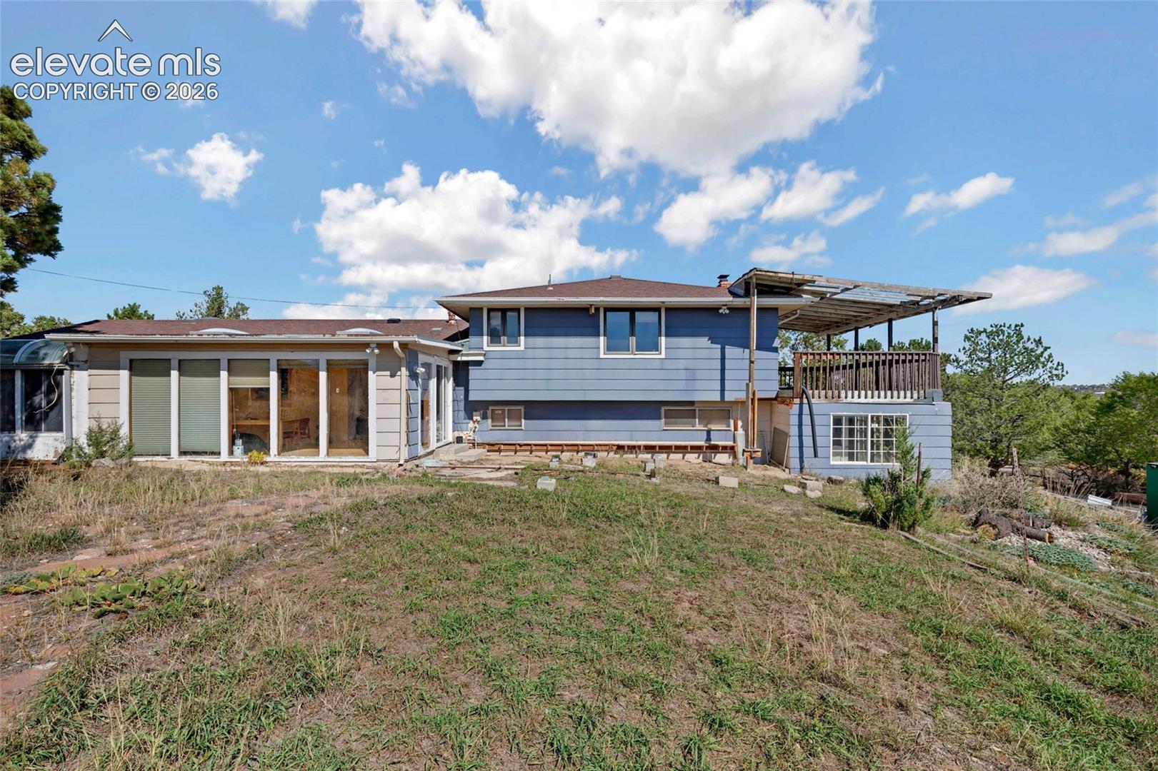 Expansive rear exterior featuring a multi-level structure with light blue siding, an attached sunroom with large windows, and an upper-level deck with a partial covering