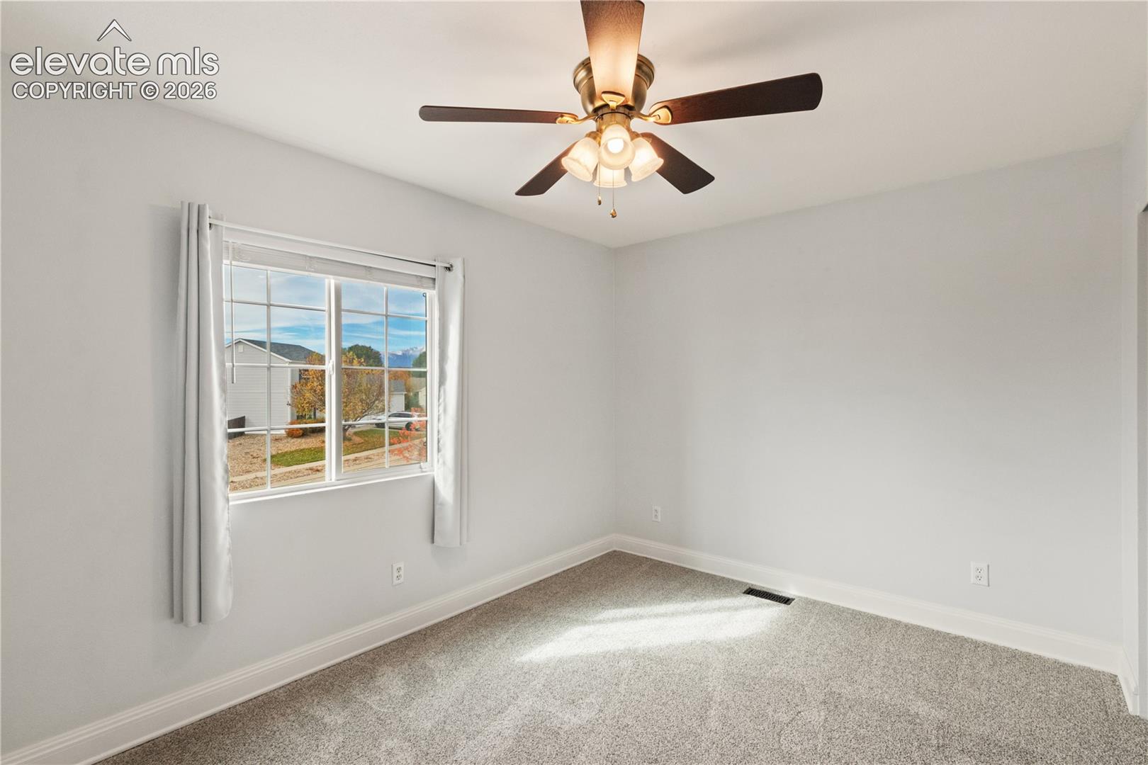 Room interior featuring wall-to-wall carpeting, a multi-pane window, and a ceiling fan with integrated lighting