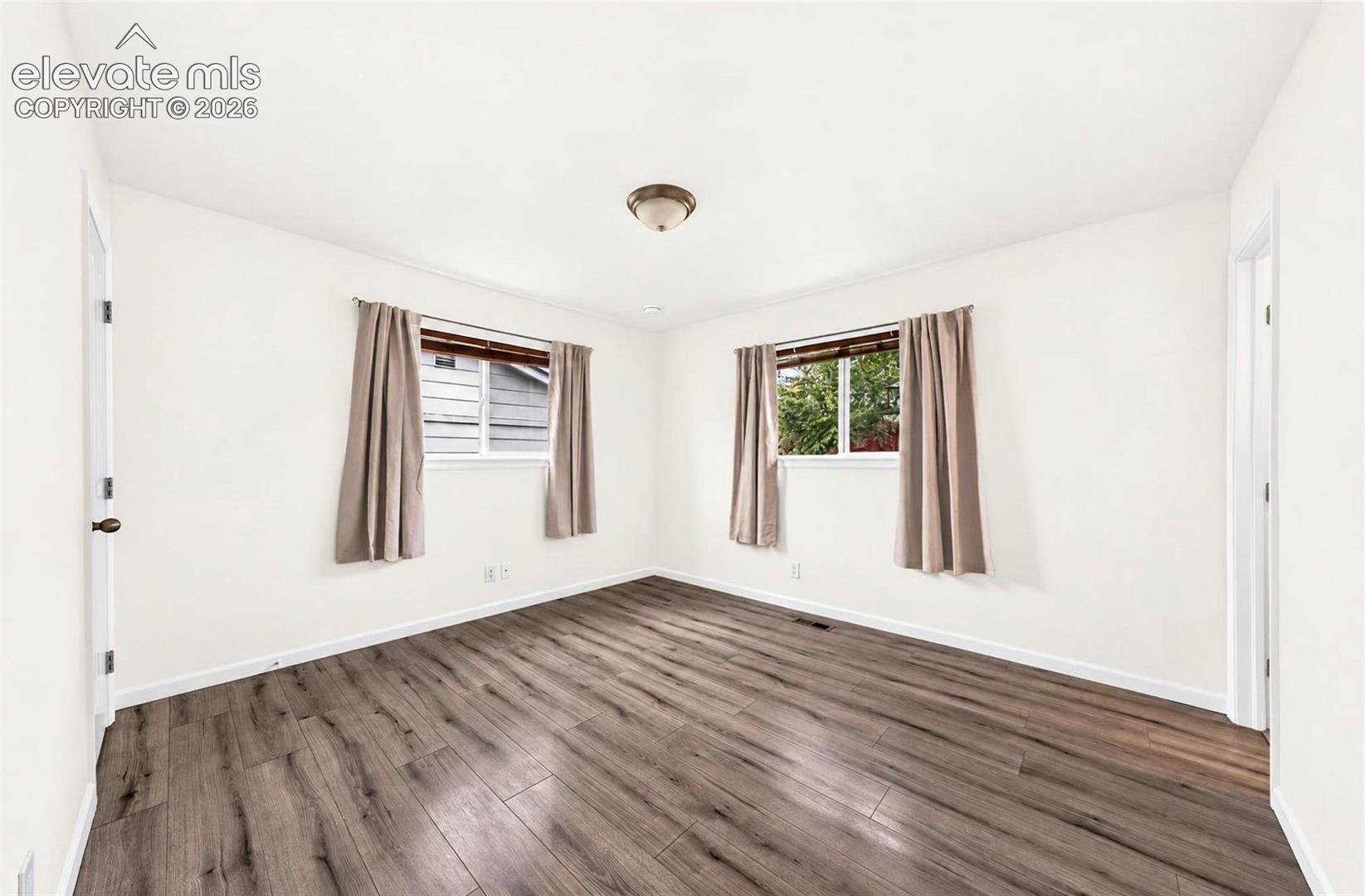 Room featuring wood-finish flooring, white walls, dual windows, and a flush-mount ceiling light fixture
