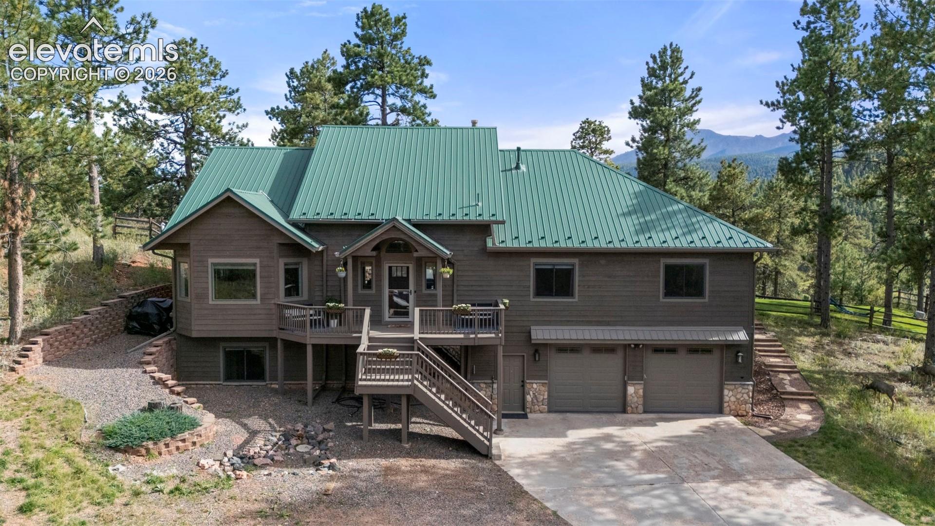 Chalet / cabin with stairs, concrete driveway, a metal roof, an attached garage, and a wooden deck