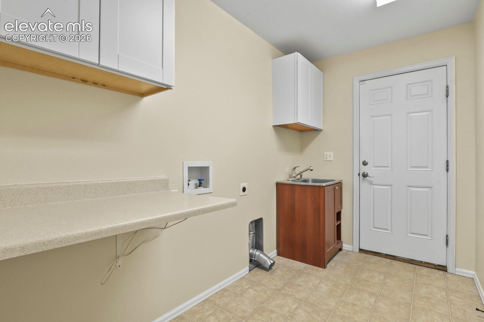 Main level Laundry room featuring a utility sink, white paneled door, tiled flooring, and door to garage