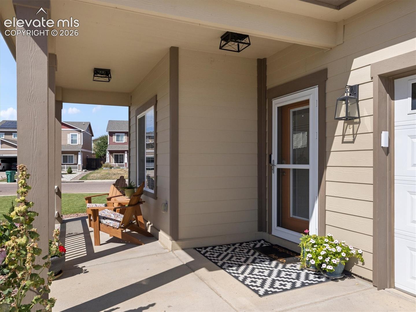 Covered front porch with concrete flooring, beige siding, and an exterior lantern sconce
