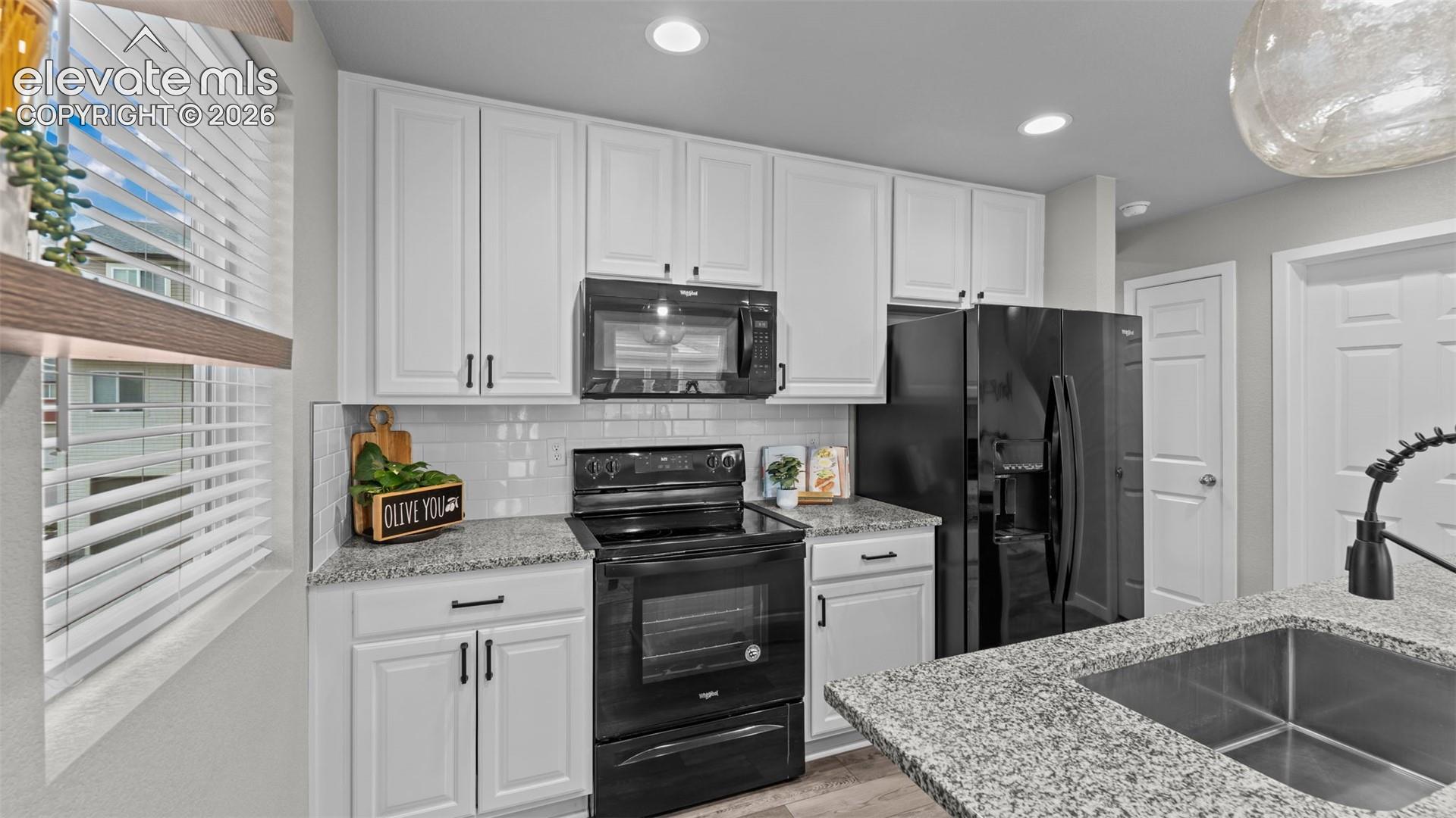 Kitchen featuring white cabinetry, stone-finish countertops, subway tile backsplash, black appliances, and stainless steel undermount sink with a pull-down faucet