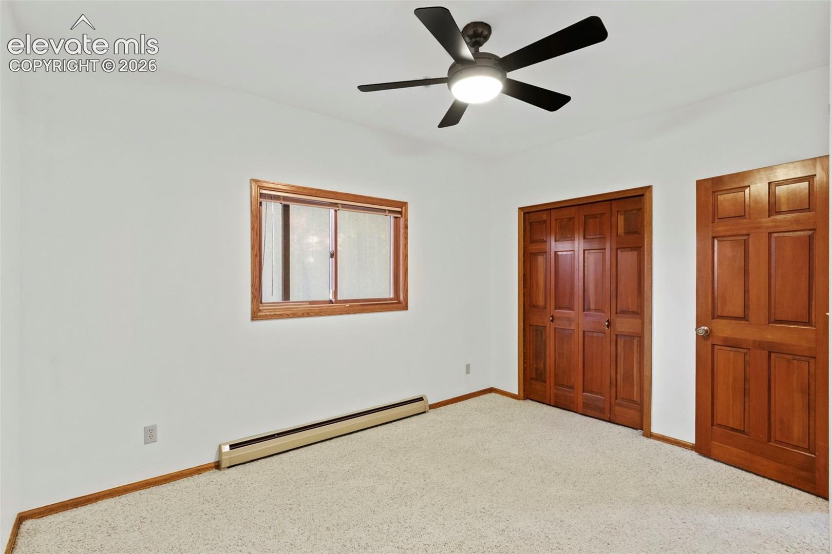 Room featuring neutral carpeting, a five-blade ceiling fan with integrated lighting, wood-trim windows, six-panel wood doors, and dual bi-fold closet doors