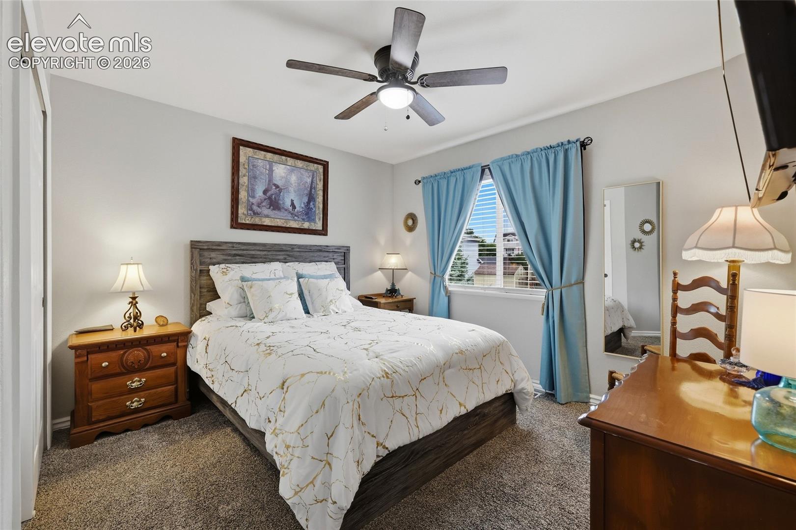 Bedroom #2 (guest room). Textured carpet flooring, ceiling fan with integrated lighting, window with blinds, and light gray wall paint