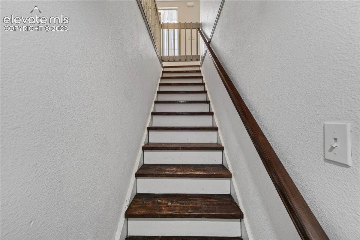 Staircase featuring dark-stained wood treads, contrasting white risers, and a wall-mounted wood handrail