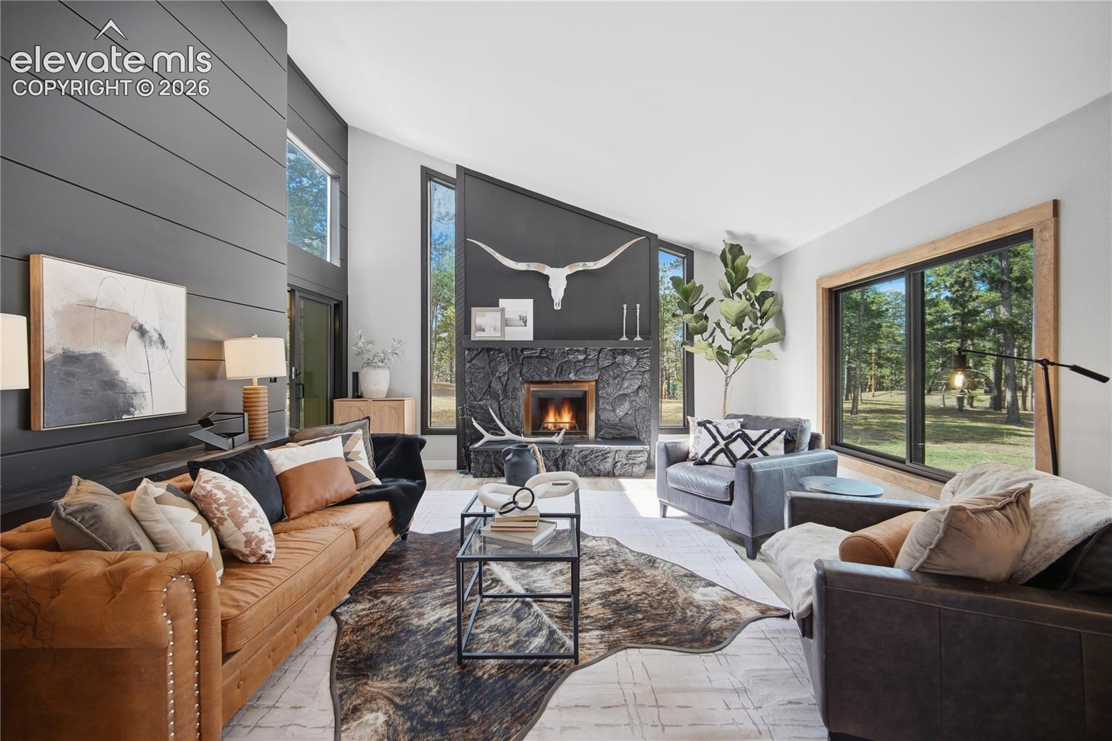 Vaulted ceilings, floor-to-ceiling stone fireplace, horizontal paneled accent wall, and expansive windows with natural wood trim