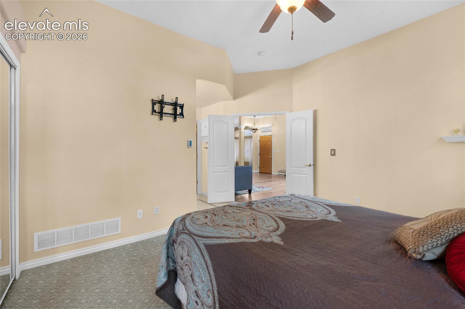 Vaulted ceiling with a centrally mounted ceiling fan, neutral wall tones, dual-panel interior doors, and closet with sliding mirrored doors