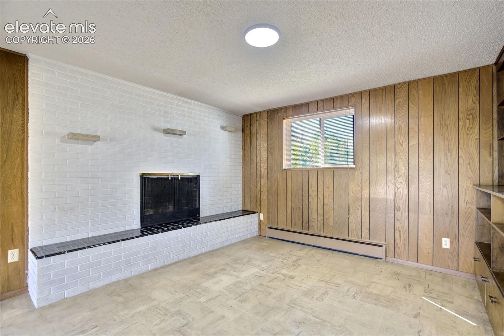Painted white brick fireplace featuring a black tile hearth, vertical wood-paneled walls, built-in shelving, and tile flooring