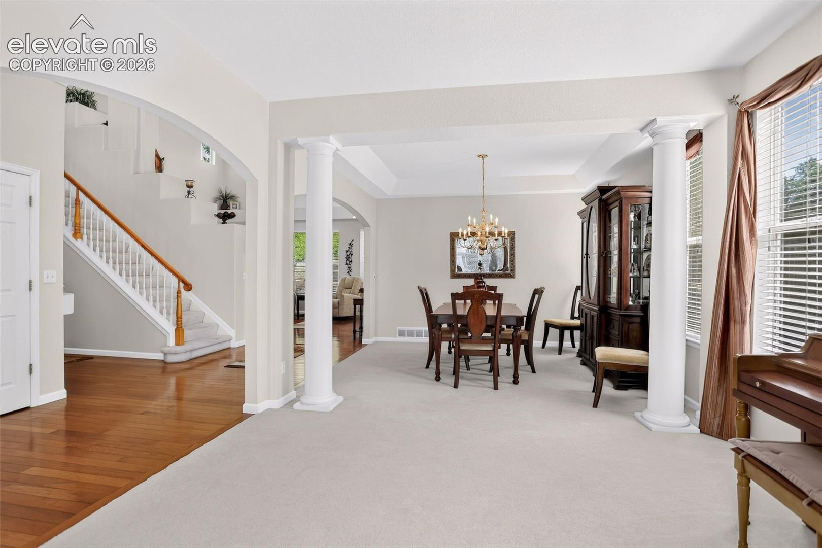 Arched doorway, wood flooring, carpeted stairs with wood handrail, columns, tray ceiling