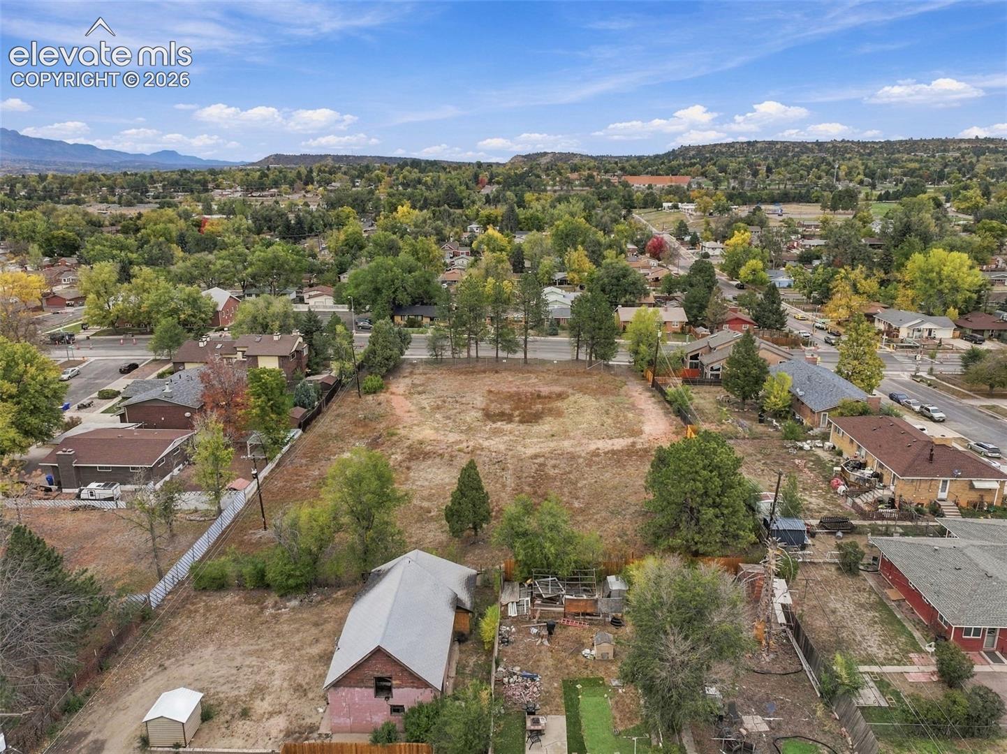 Expansive vacant lot featuring mature trees, mountain backdrop, and established perimeter fencing