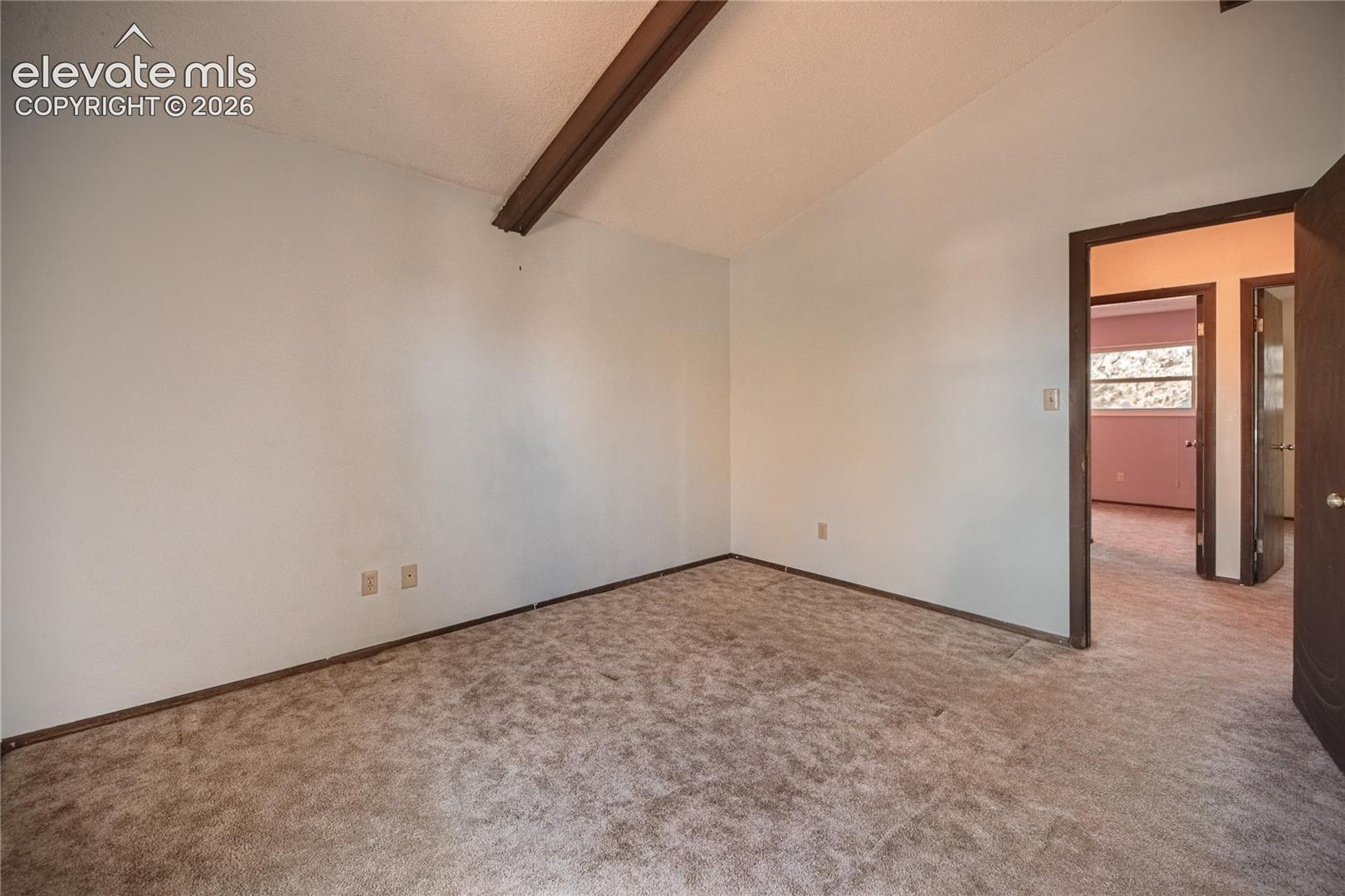 Vaulted ceiling featuring an exposed decorative wood beam and neutral wall-to-wall carpeting