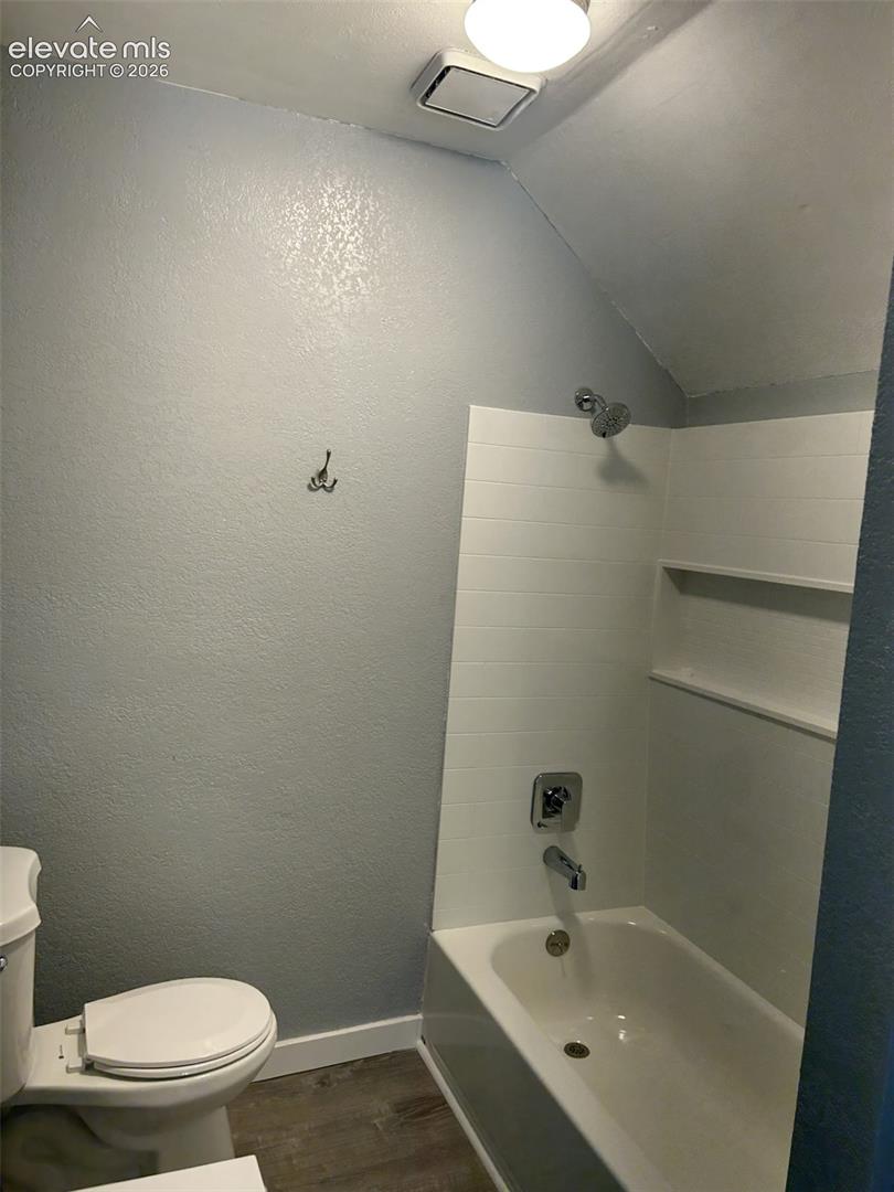 White bathtub with chrome fixtures, integrated shelving, and wood-finish flooring