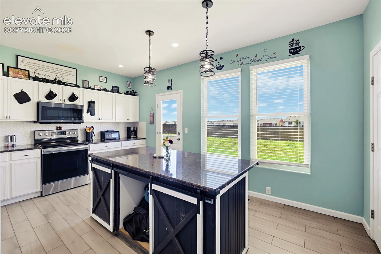 Kitchen featuring a central island with a dark countertop, white cabinetry, stainless steel appliances, wood-finish flooring, and natural light from multiple windows