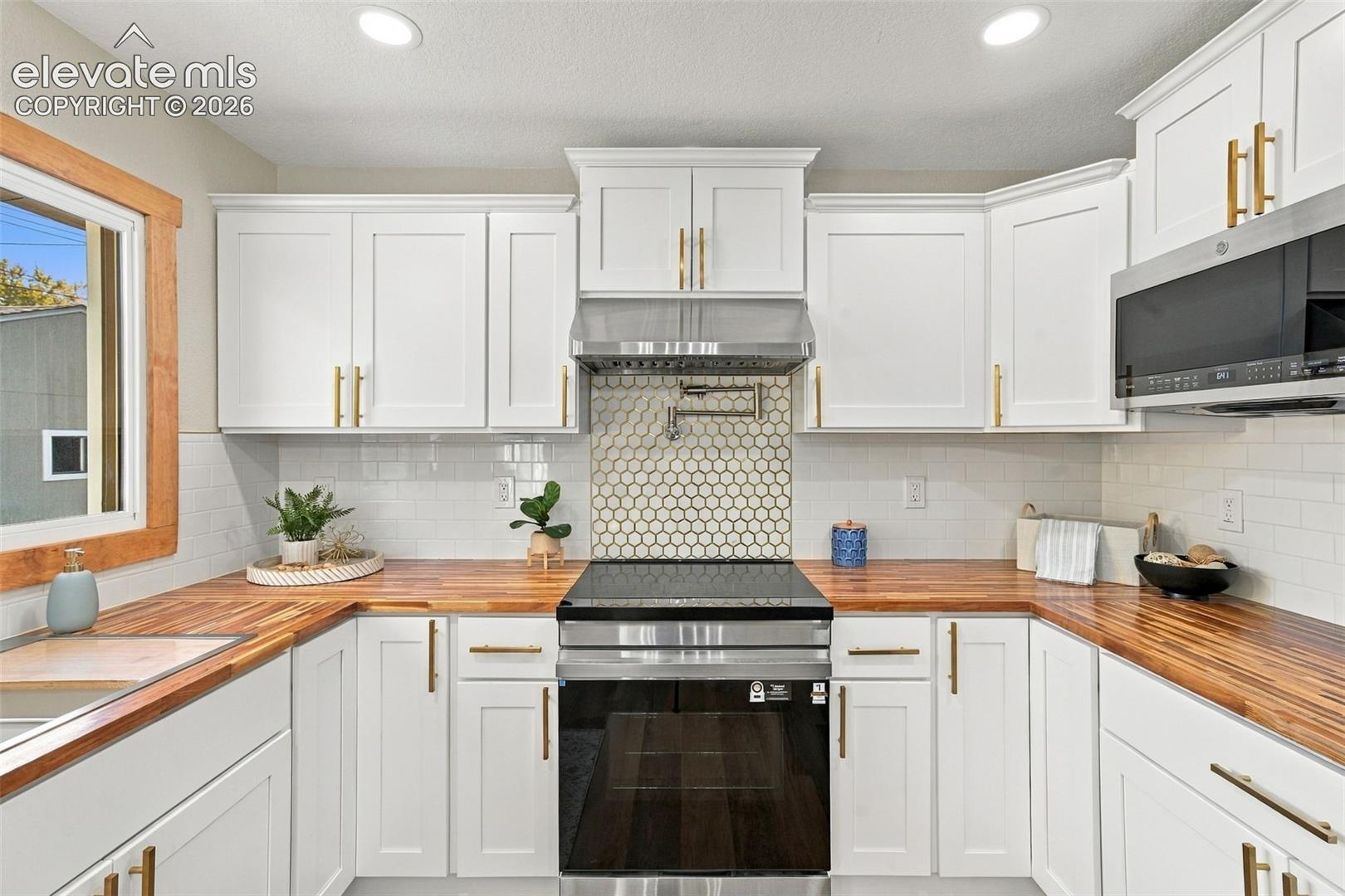Kitchen featuring white shaker-style cabinetry, wood-finish countertops, stainless steel appliances, a hexagonal tile backsplash, and metallic hardware