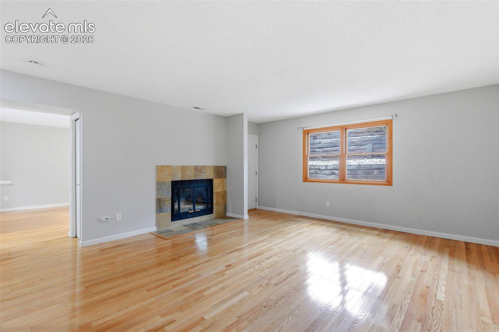 Living area featuring light wood-finish flooring, a tile-surround fireplace with a dark insert, a wood-framed window, and neutral wall paint