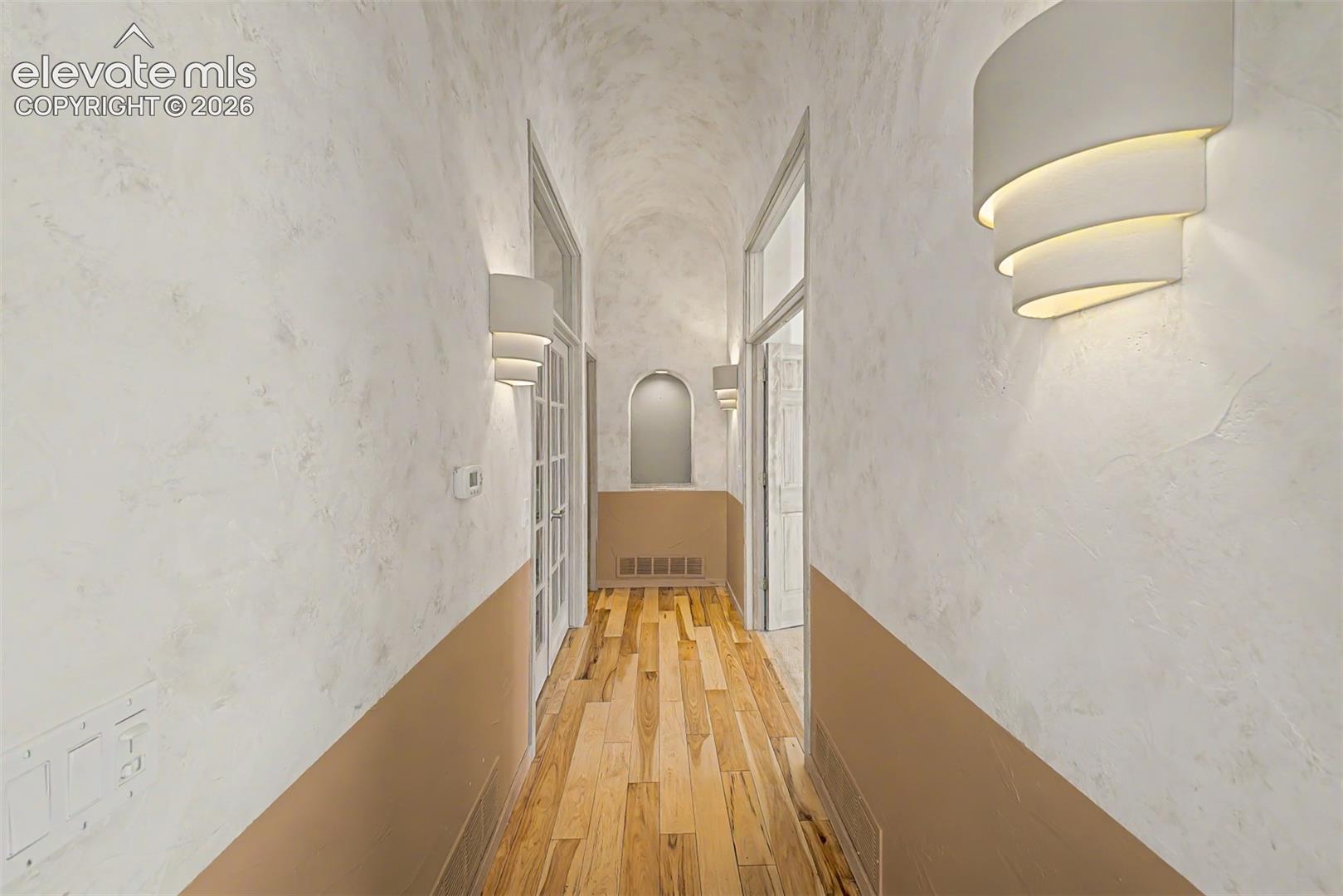 Vaulted ceiling with textured finish, wood-finish flooring, and contemporary wall sconces