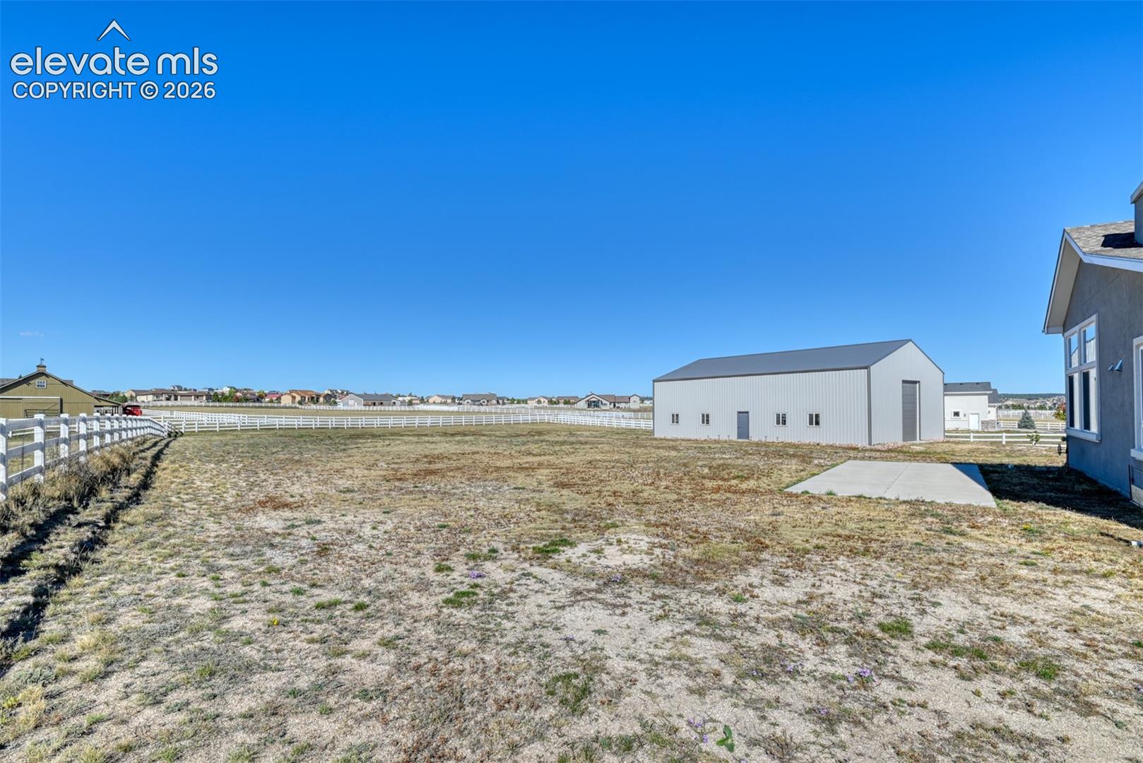 Expansive lot with a white split rail fence, pole barn outbuilding, RV concrete pad with hook ups.