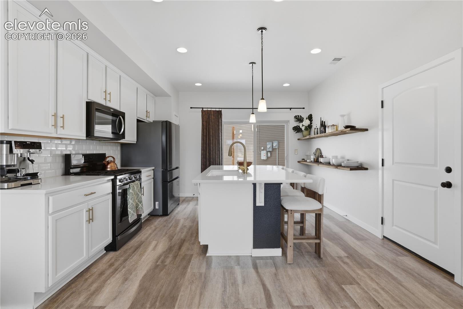 Modern kitchen with white cabinetry and gold-tone hardware, featuring a white subway tile backsplash and black appliances