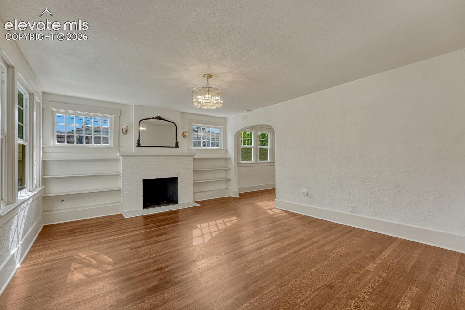 Wood-finish flooring, built-in shelving, white fireplace, chandelier, and archway entryway