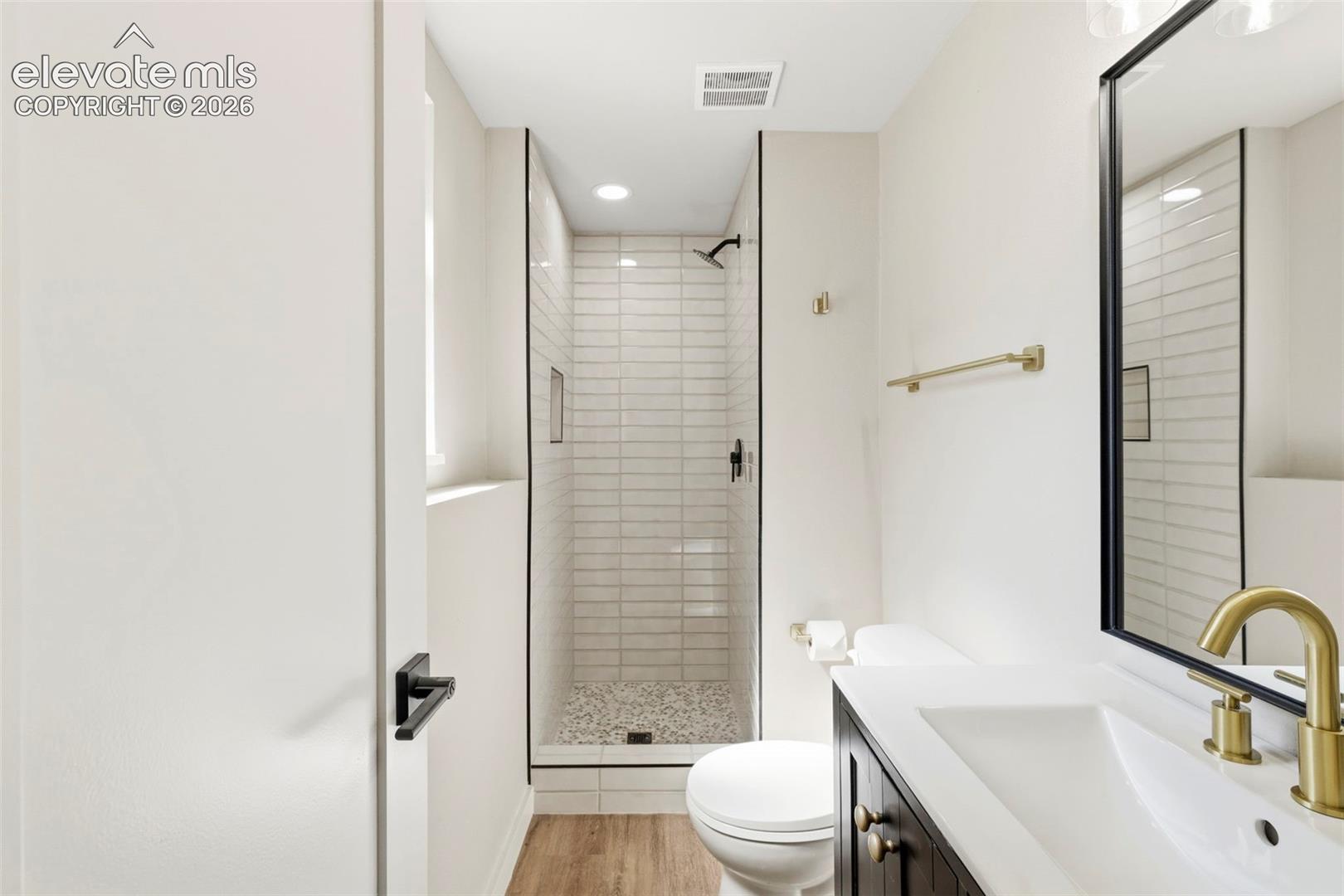 Modern bathroom featuring a walk-in shower with subway tile surround, sleek black-framed mirror, and a vanity with a white countertop and gold-toned fixtures