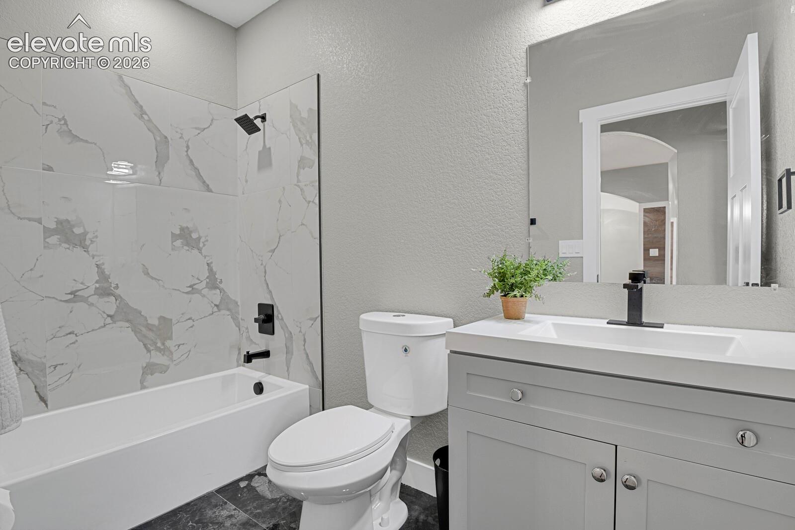 Bathroom featuring a shaker-style vanity with a rectangular sink, large-format tile shower surround with marble-finish detailing, matte black plumbing fixtures, and a frameless wall mirror