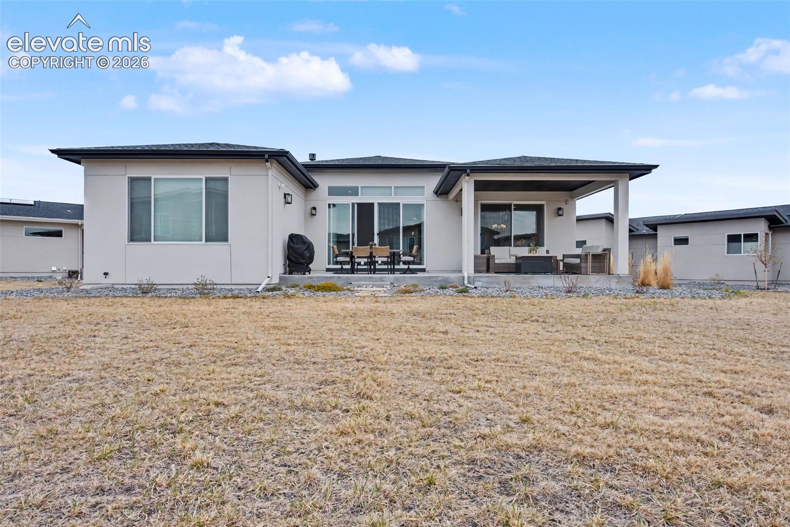 Rear view of property with a patio area, stucco siding, and a yard