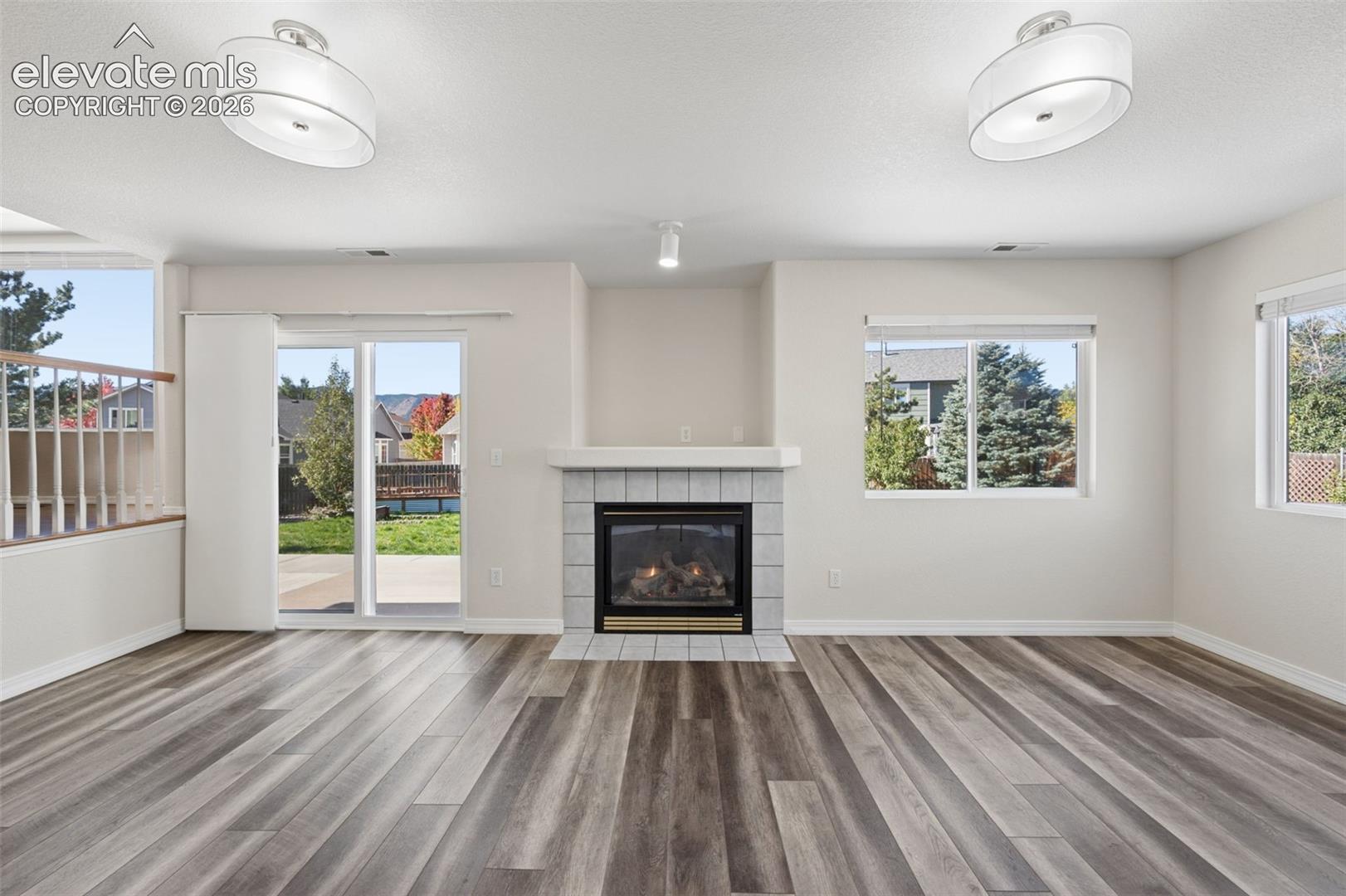 Living area featuring wood-finish flooring, a tile-surround fireplace with a mantel, two drum-style ceiling light fixtures, and a sliding glass door