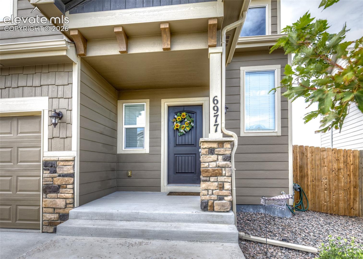 Covered entryway featuring stone-veneer column bases, decorative corbel accents, composite lap siding, and a paneled entry door