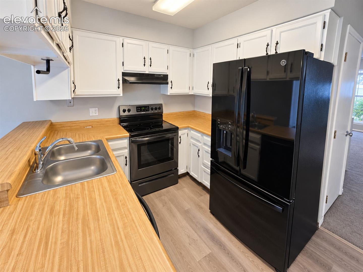 Kitchen featuring white cabinetry with black hardware, wood-finish laminate countertops, a double-basin stainless steel sink, black range, and black refrigerator