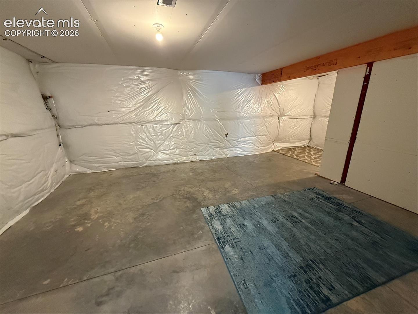 Unfinished interior space featuring concrete flooring, exposed wooden ceiling joists, and insulated wall coverings