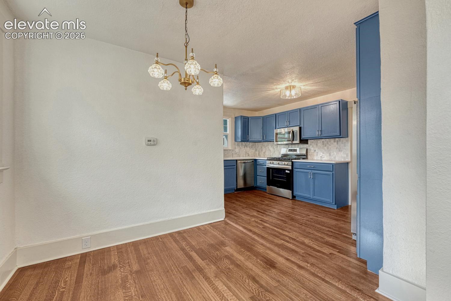 Hardwood flooring throughout, with a brass chandelier, and a kitchen featuring blue cabinetry, stainless steel appliances, and a tile backsplash