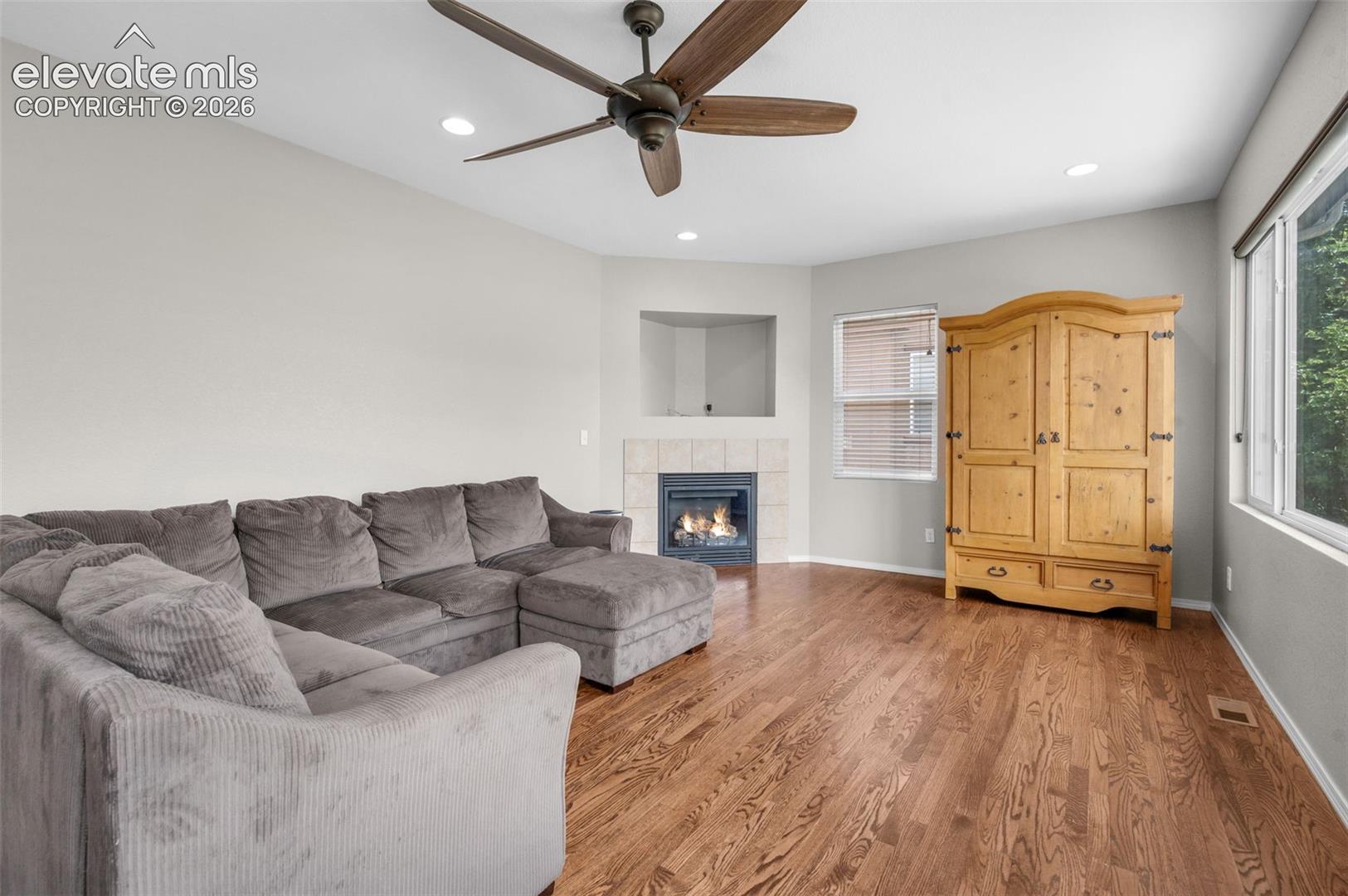 Spacious living area featuring wood-finish flooring, a corner gas fireplace with tile surround, recessed lighting, and a ceiling fan.