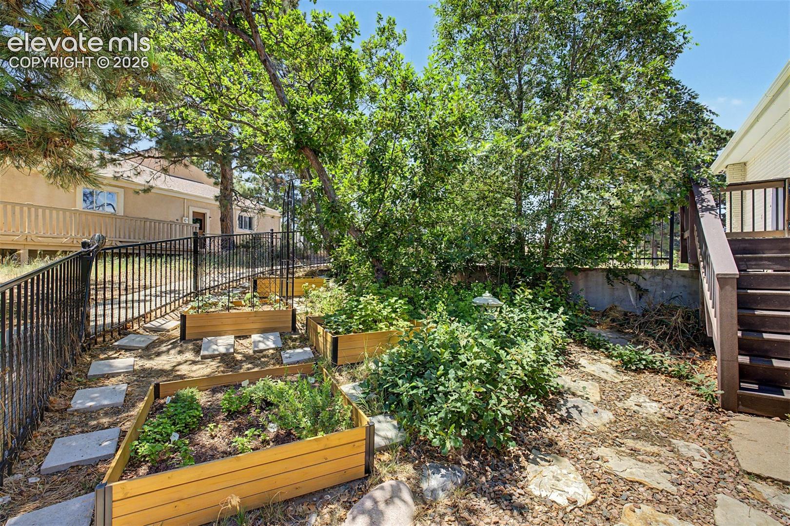 Tucked along a stone path and wrought-iron fence line, a series of raised garden beds offers a ready-made spot for growing herbs and vegetables, shaded by mature trees on this gently sloping corner of the lot.